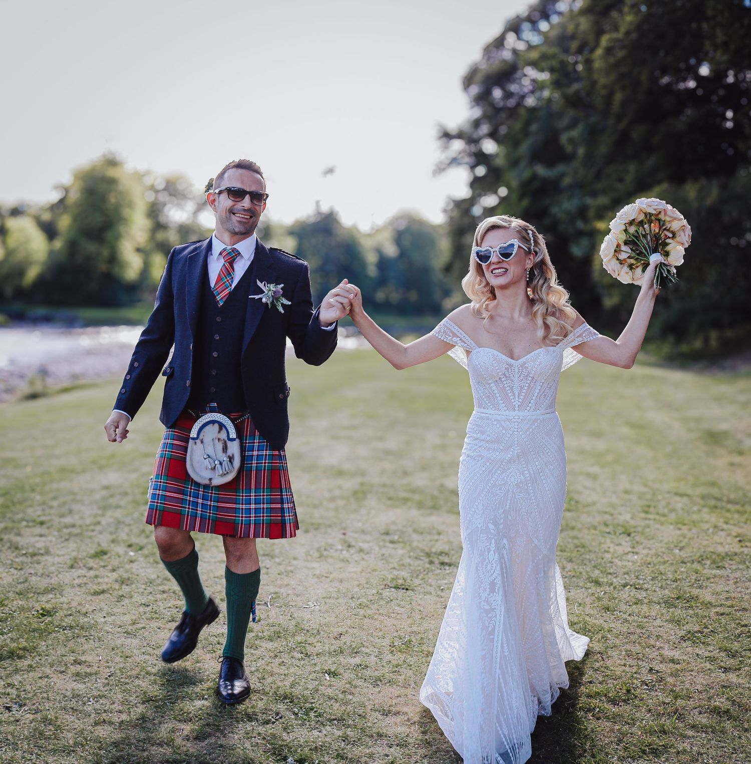 A couple in wedding attire dances and spins together on a grassy hillside at sunset.
