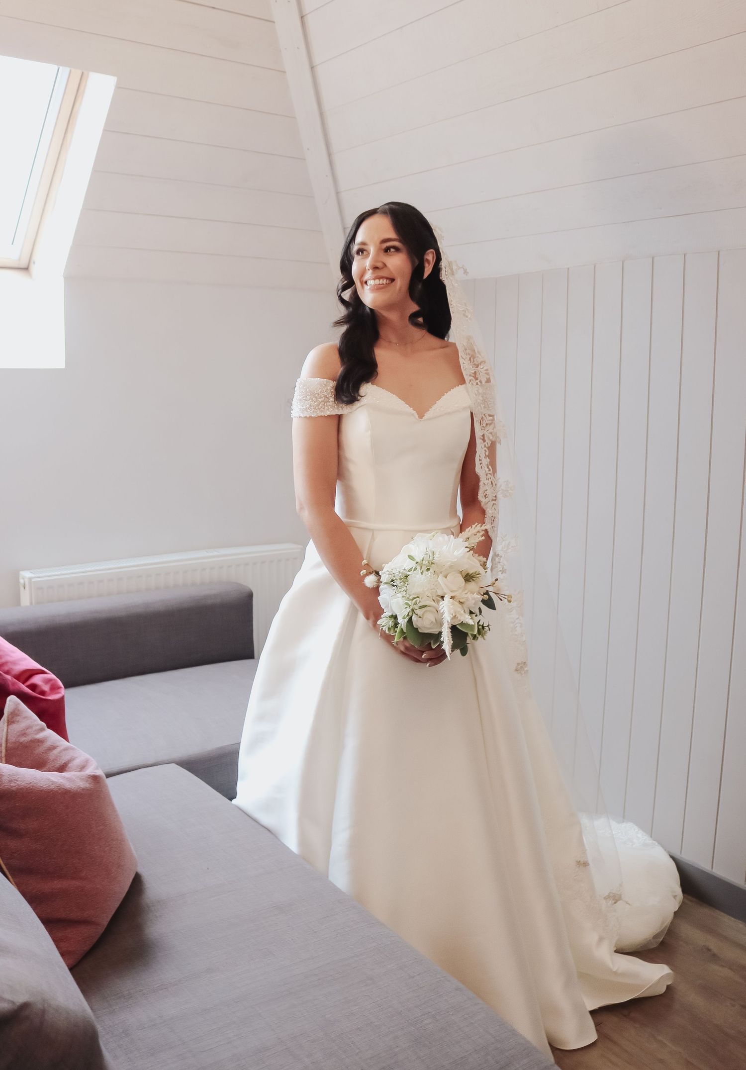 A bride in a classic white wedding dress poses gracefully in a bright room with white paneled walls and pink accents.
