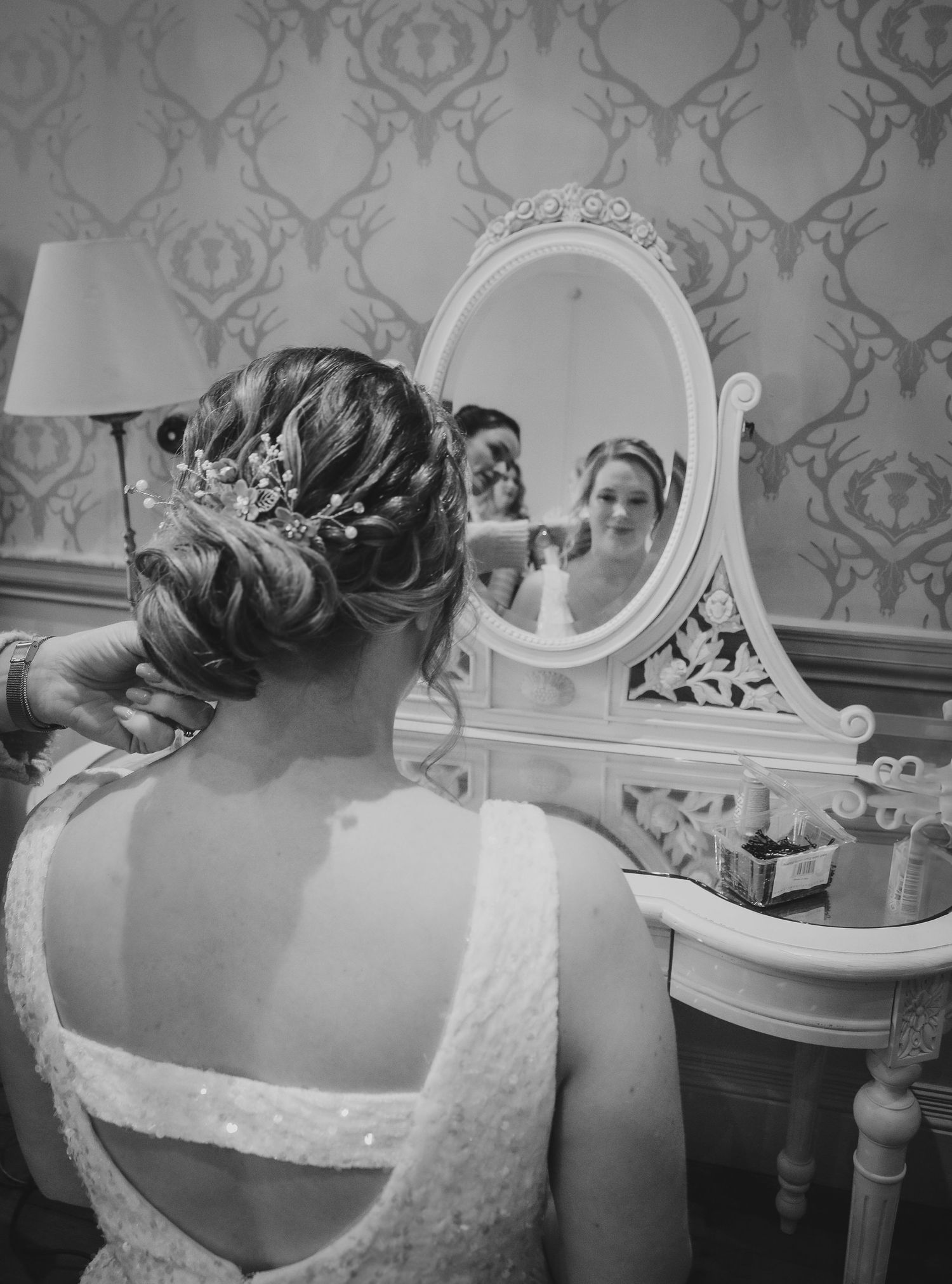 A black and white wedding photo showing someone looking into an ornate vintage vanity mirror wearing a lace dress.