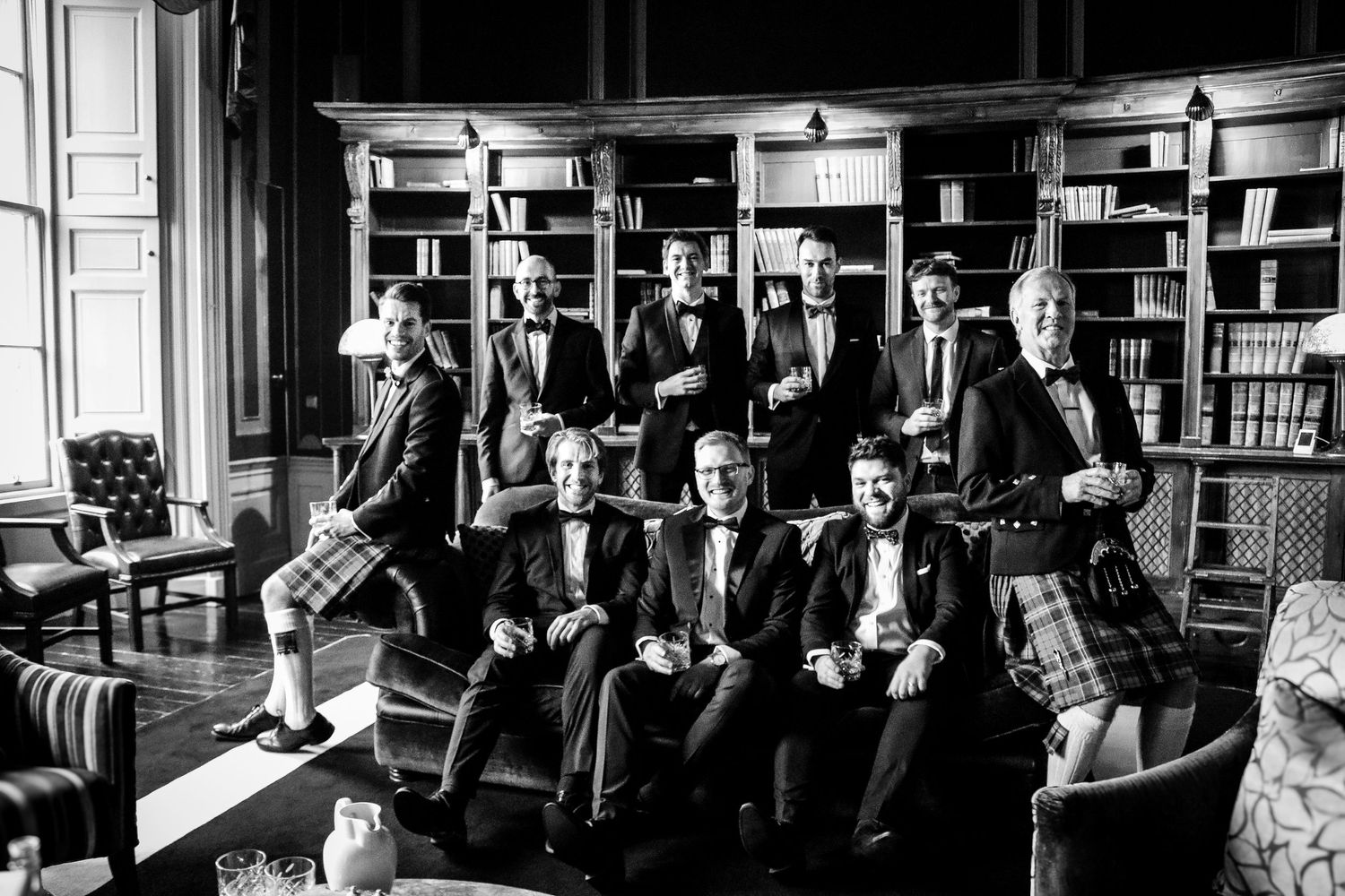 Black and white photograph of a group of formally dressed people posing in a library or study room setting.