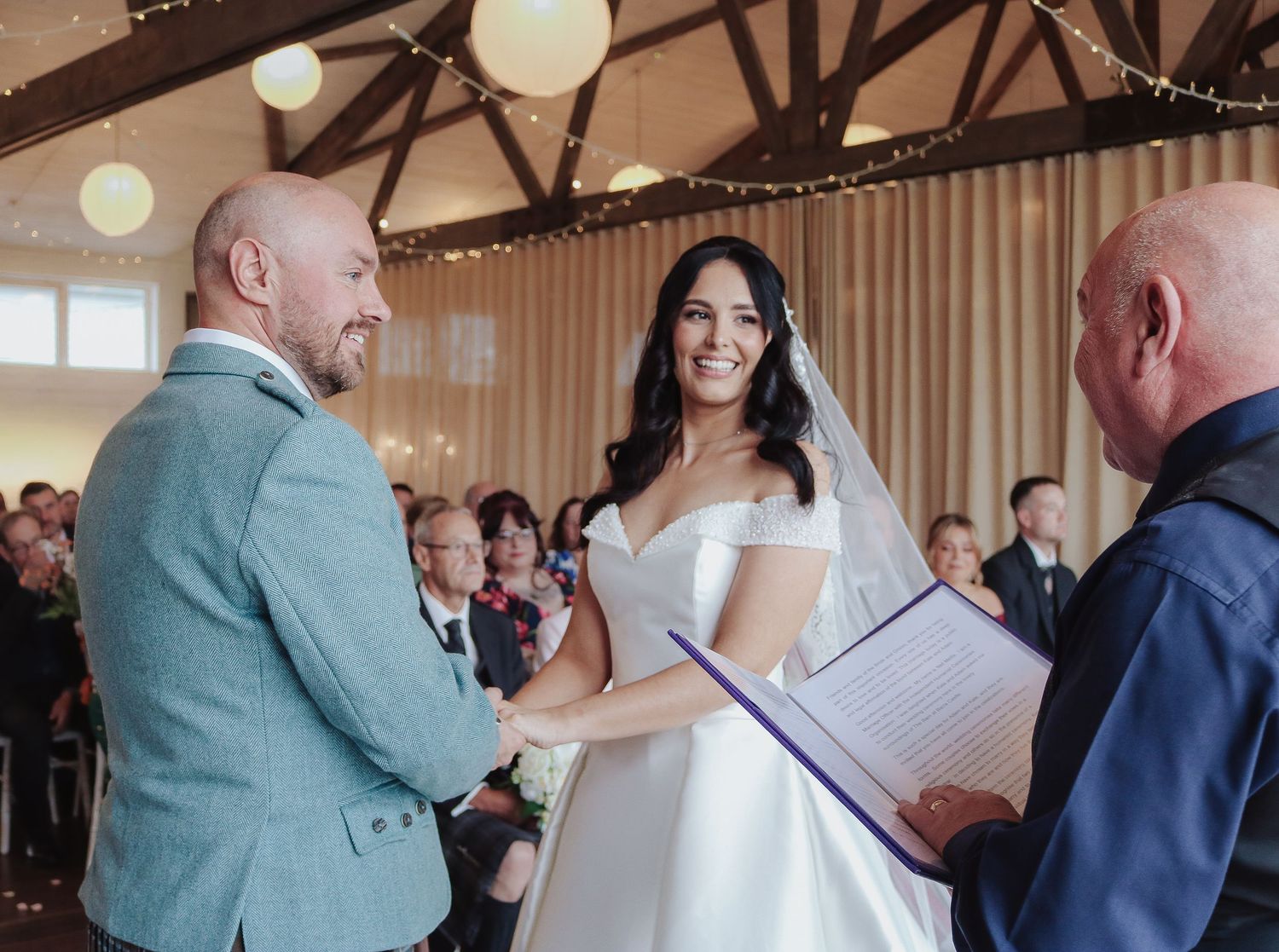 A joyful wedding ceremony takes place indoors with a couple exchanging vows in front of an officiant.