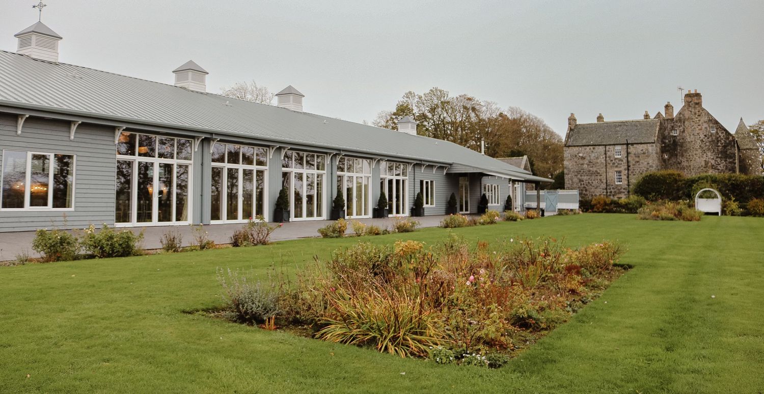 Rolling green hills and gardens surround a stately white building on a cloudy day.