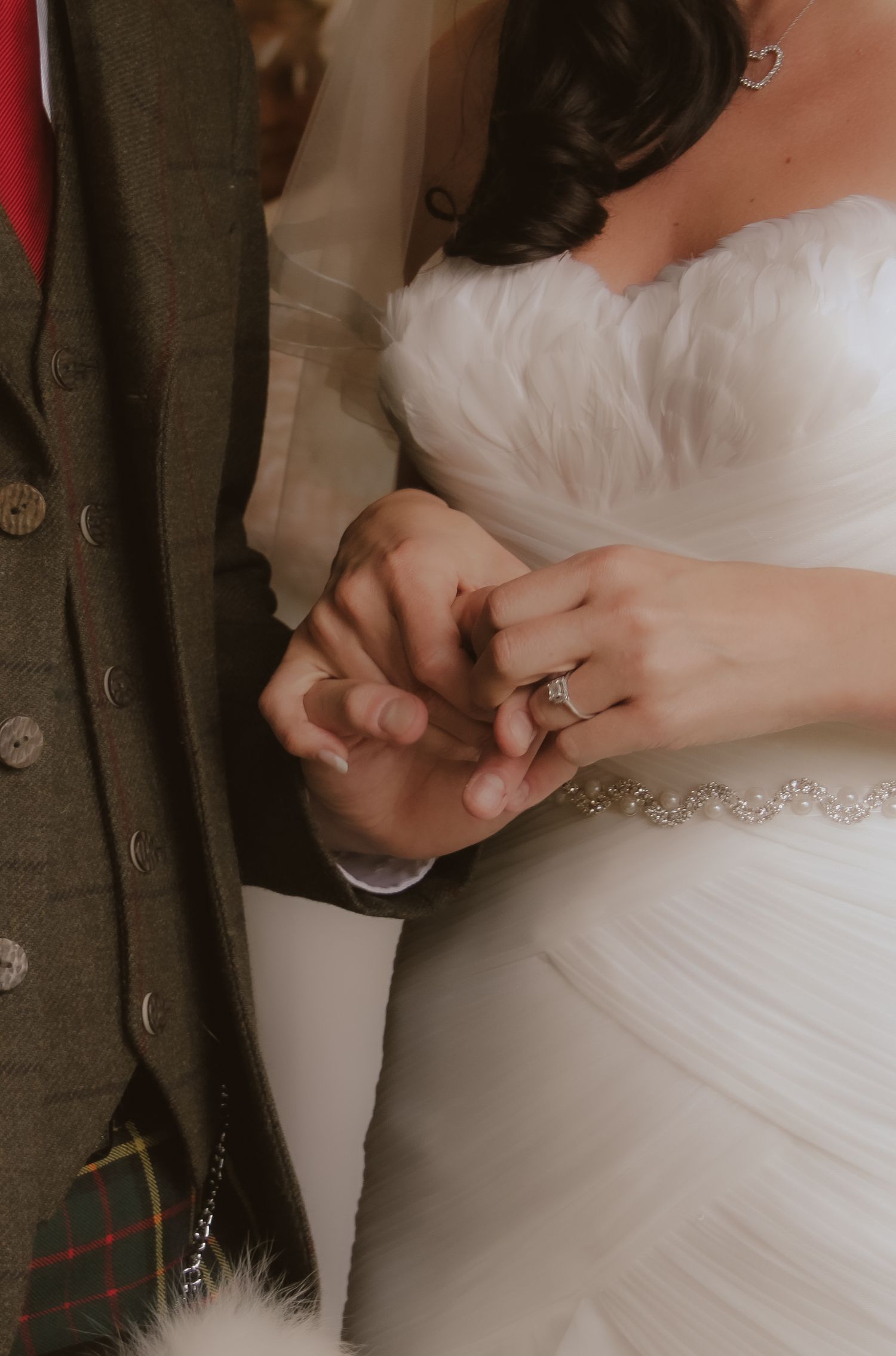 Close-up of wedding dress details and ring in warm lighting.