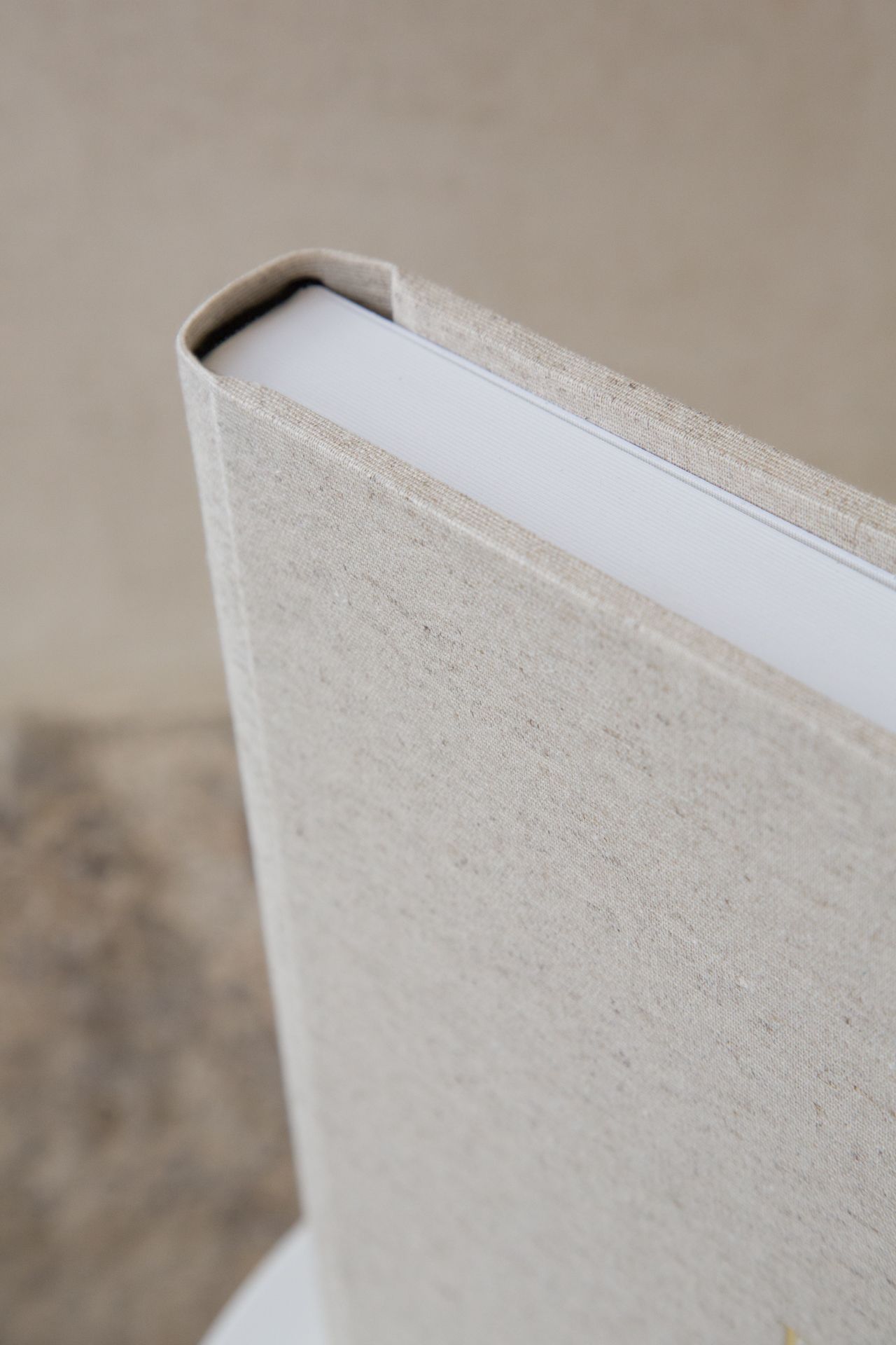 Close-up view of a hardcover book spine showing textured beige cloth binding and white pages inside.