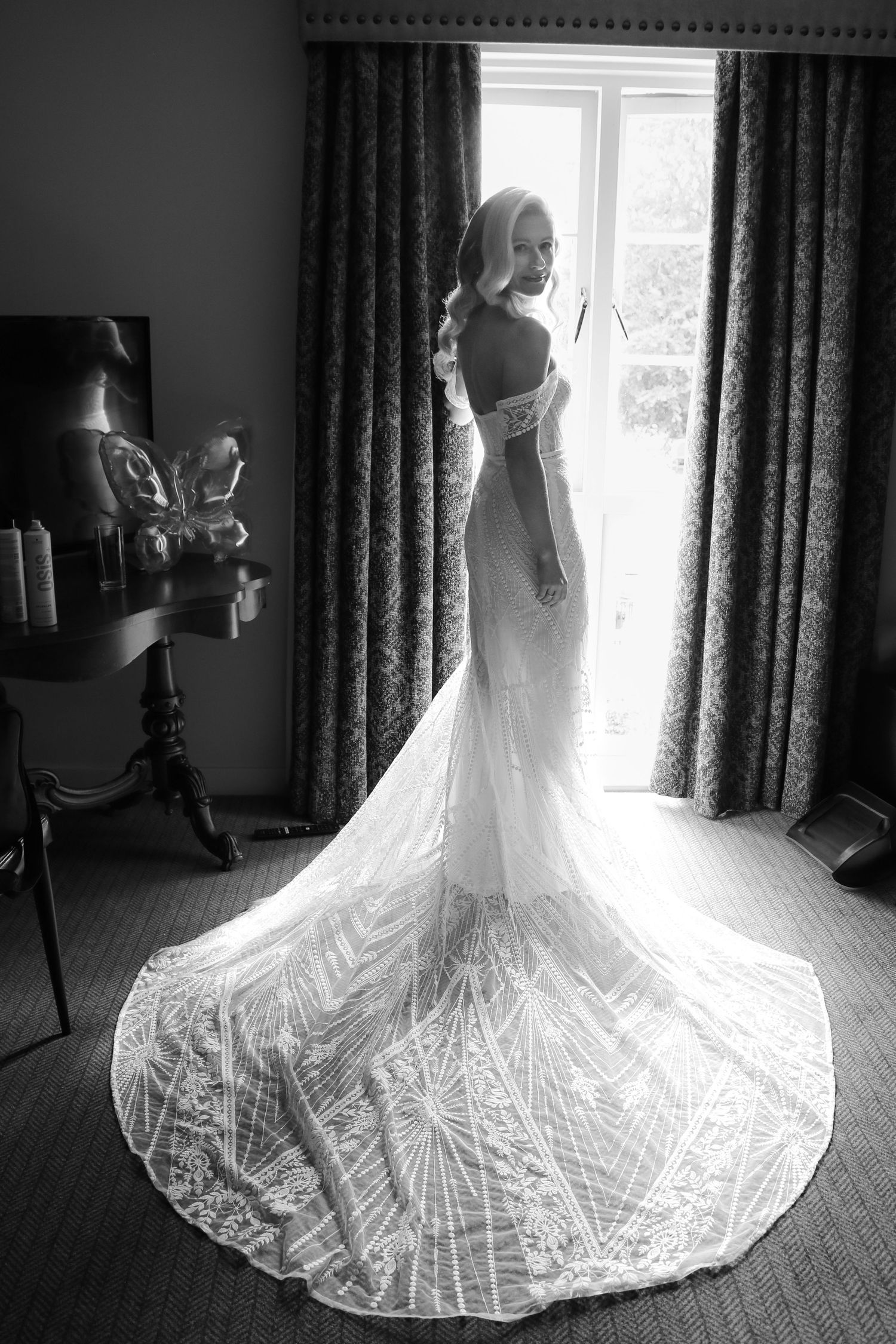 A wedding dress with a long intricate lace train is backlit by window light in a series of elegant silhouette photos.