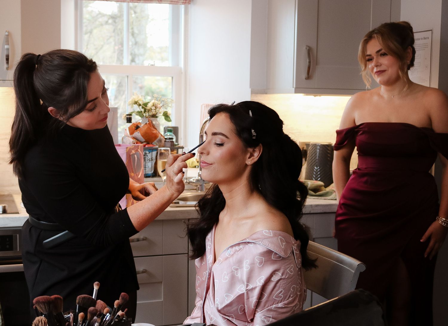 Behind-the-scenes view of makeup artist applying cosmetics to model in natural window light.