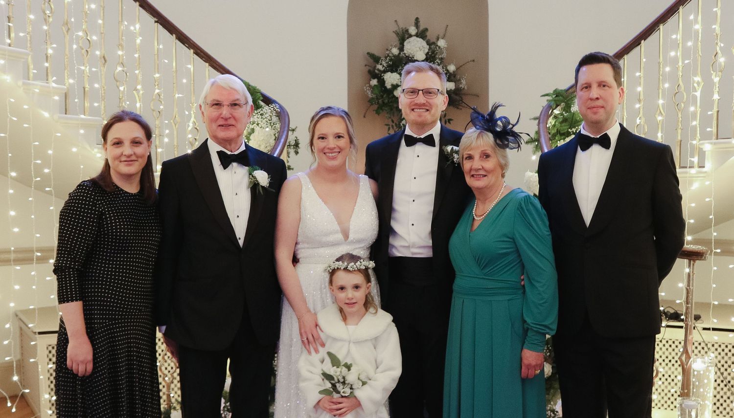 Wedding party members in formal attire including tuxedos and gowns pose together at an elegant holiday-themed celebration.