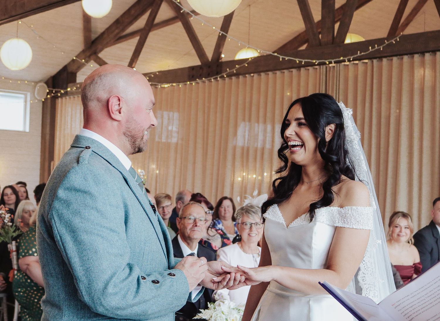 A couple shares their first dance together at a rustic wedding reception venue with wooden beams and white draping.