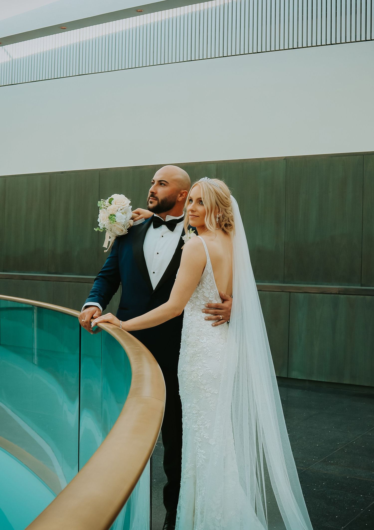 A bride and groom share an intimate moment by a modern pool deck with geometric architecture and turquoise water.