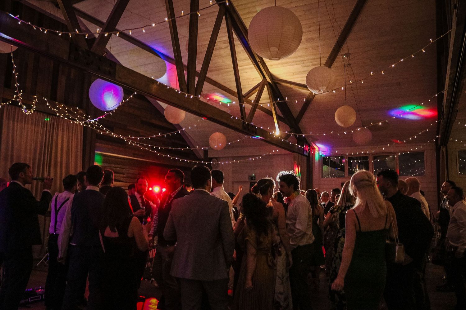 People dancing and socializing at a dimly lit party venue decorated with string lights and paper lanterns.