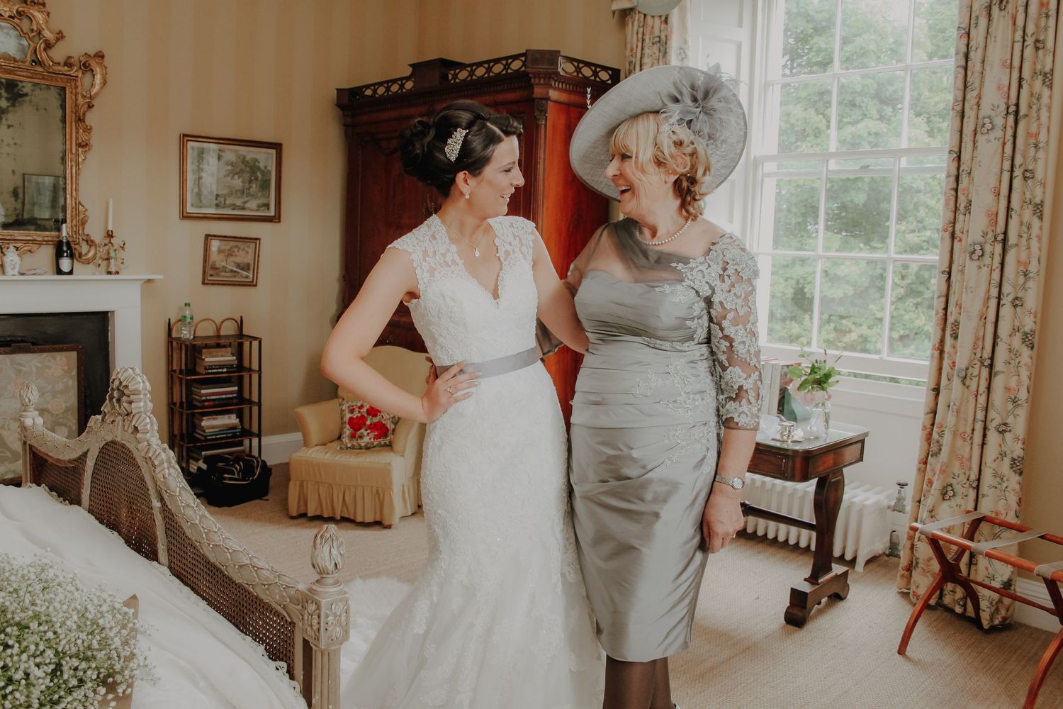 Two people in formal attire share a joyful moment in an elegant living room with vintage furnishings and natural light.