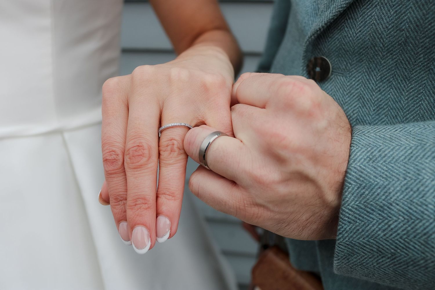 Close-up view of hands exchanging wedding rings during a ceremony with a teal colored suit jacket visible.