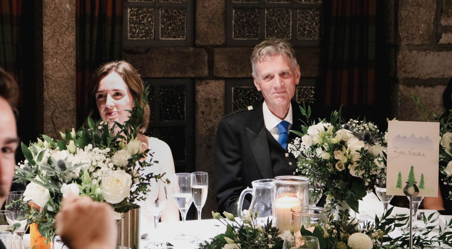 Wedding reception dinner with elegant white floral table centerpieces and candle decorations at a rustic venue.