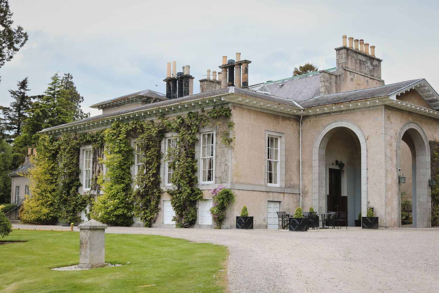 Ivy-covered Georgian country house with gravel driveway, manicured lawns, and elegant arched entrance portico.