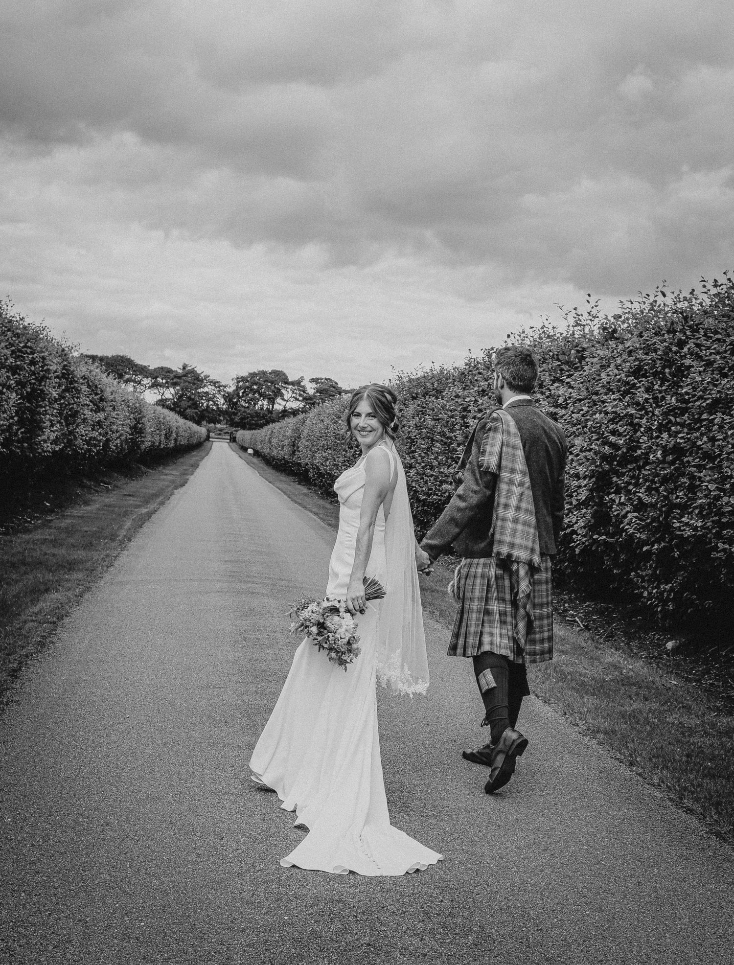 A wedding couple walks along a tree-lined country road near Elsick House in Aberdeenshire