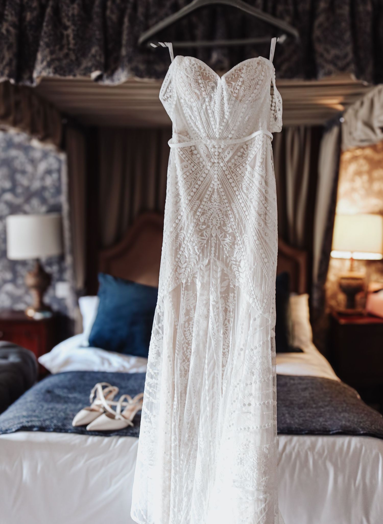 Detail shots of a white lace wedding dress hanging against a dark bedroom backdrop with blue accents and bedding.