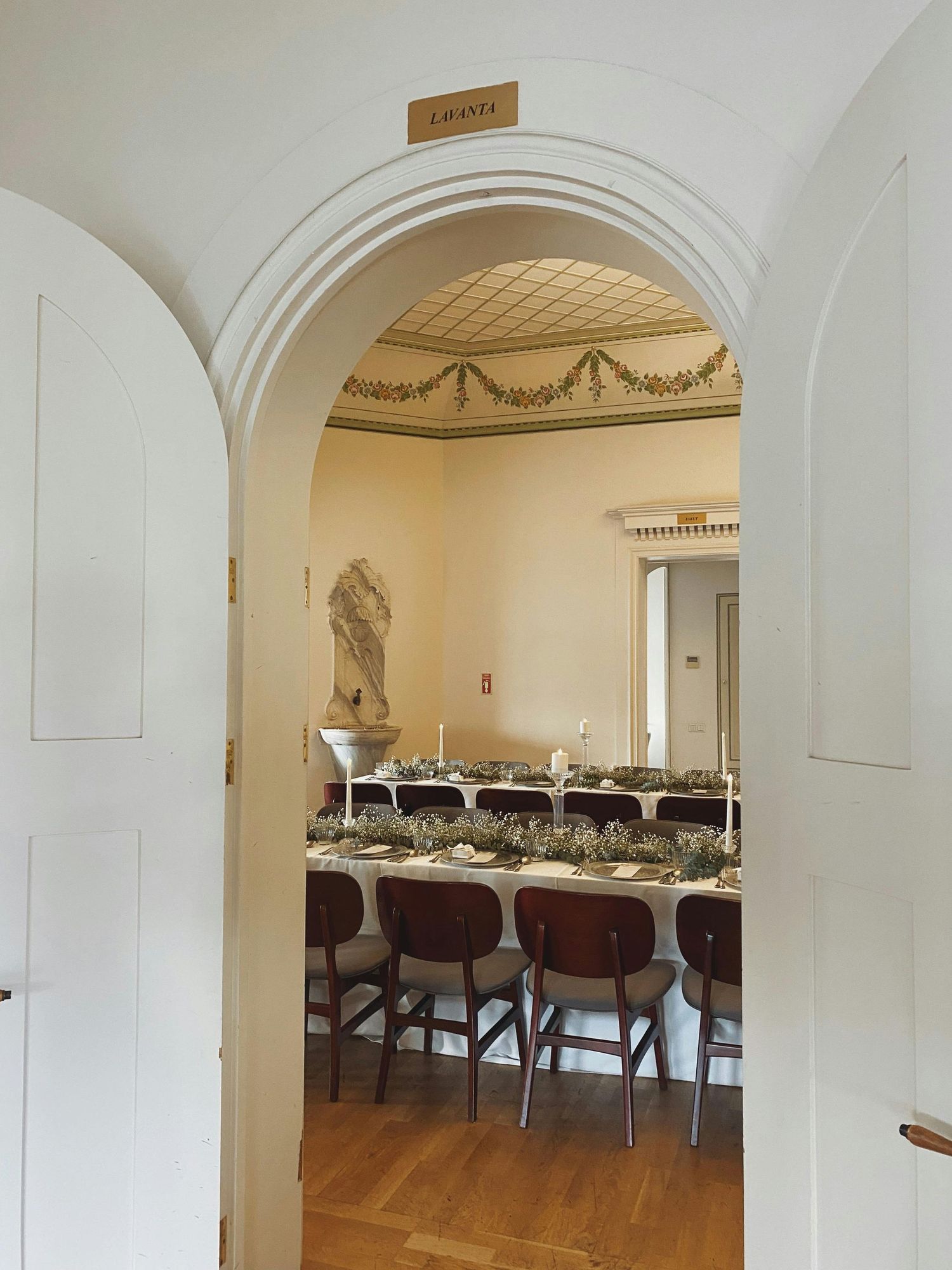 Interior view of an elegant museum gallery with arched doorways and classical sculptures displayed in white-walled spaces.