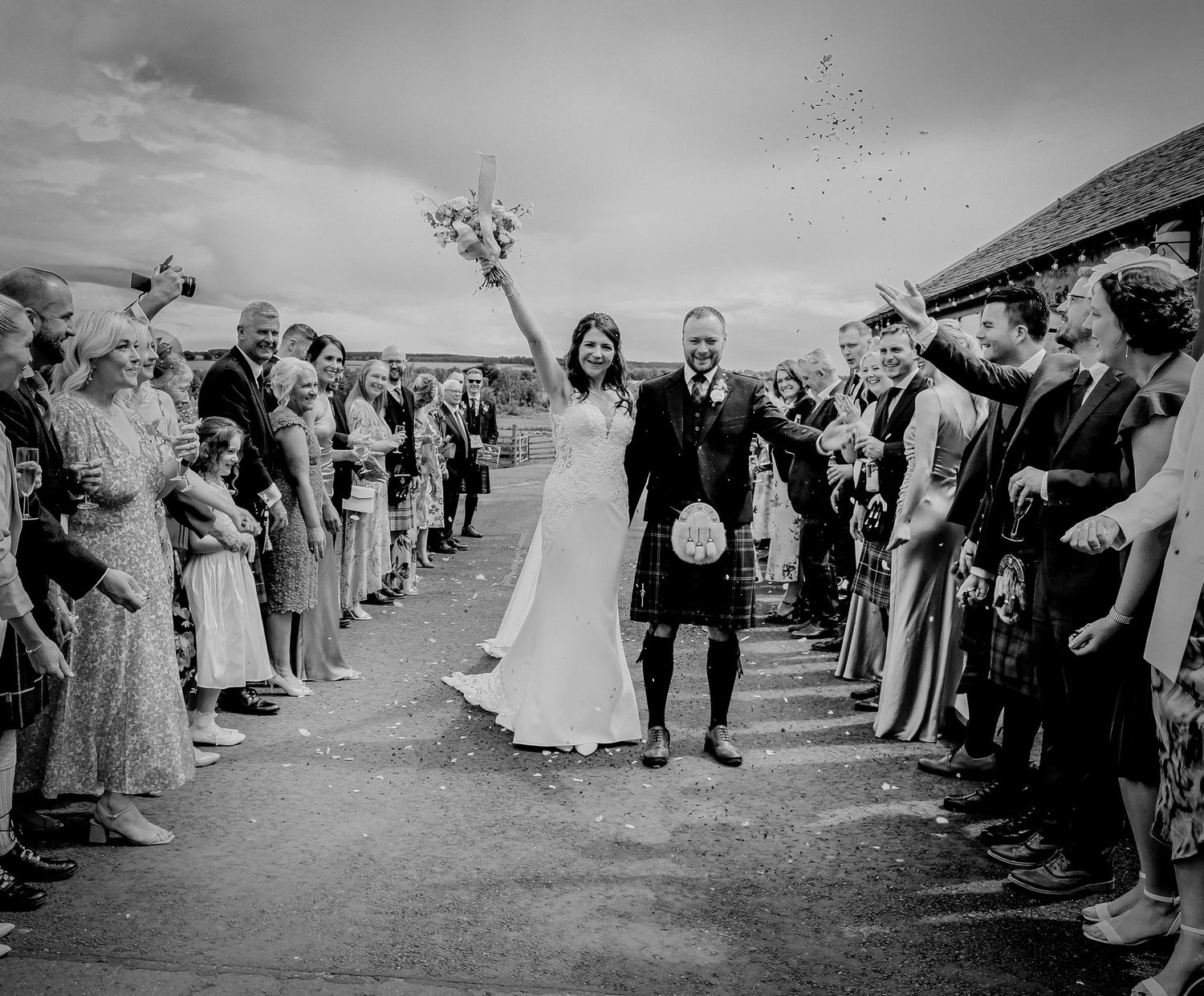 Guests throw confetti over a newlywed couple walking down the path at a Scottish Highland wedding celebration.