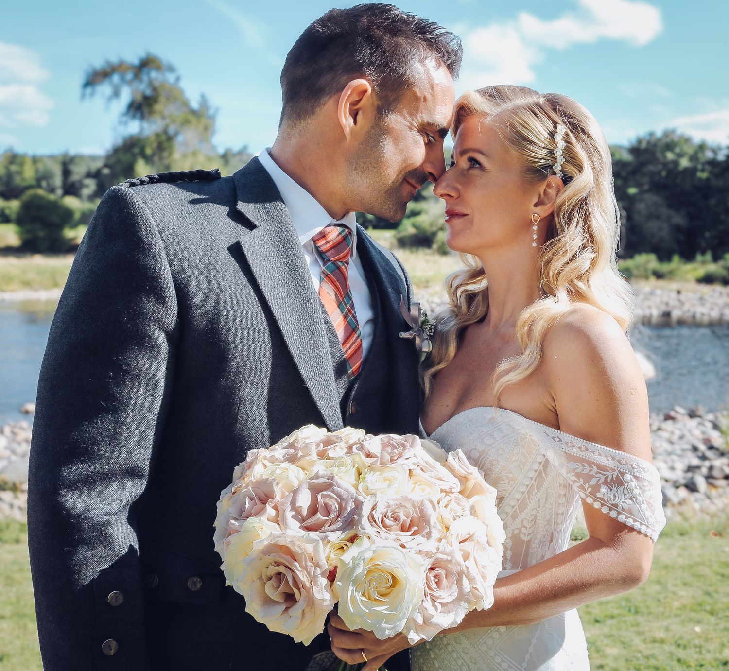 Romantic wedding couple shares tender moments by the water with pink and white rose bouquet.
