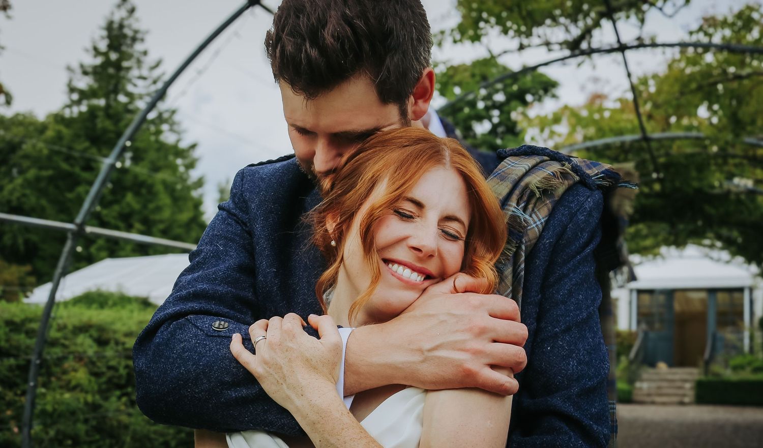A romantic couple shares an intimate embrace in a lush outdoor garden setting during a wedding photoshoot.