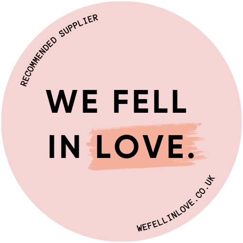 Pink circular logo design with black text reading 'WE FELL IN LOVE' and a peach-colored accent bar on white background.