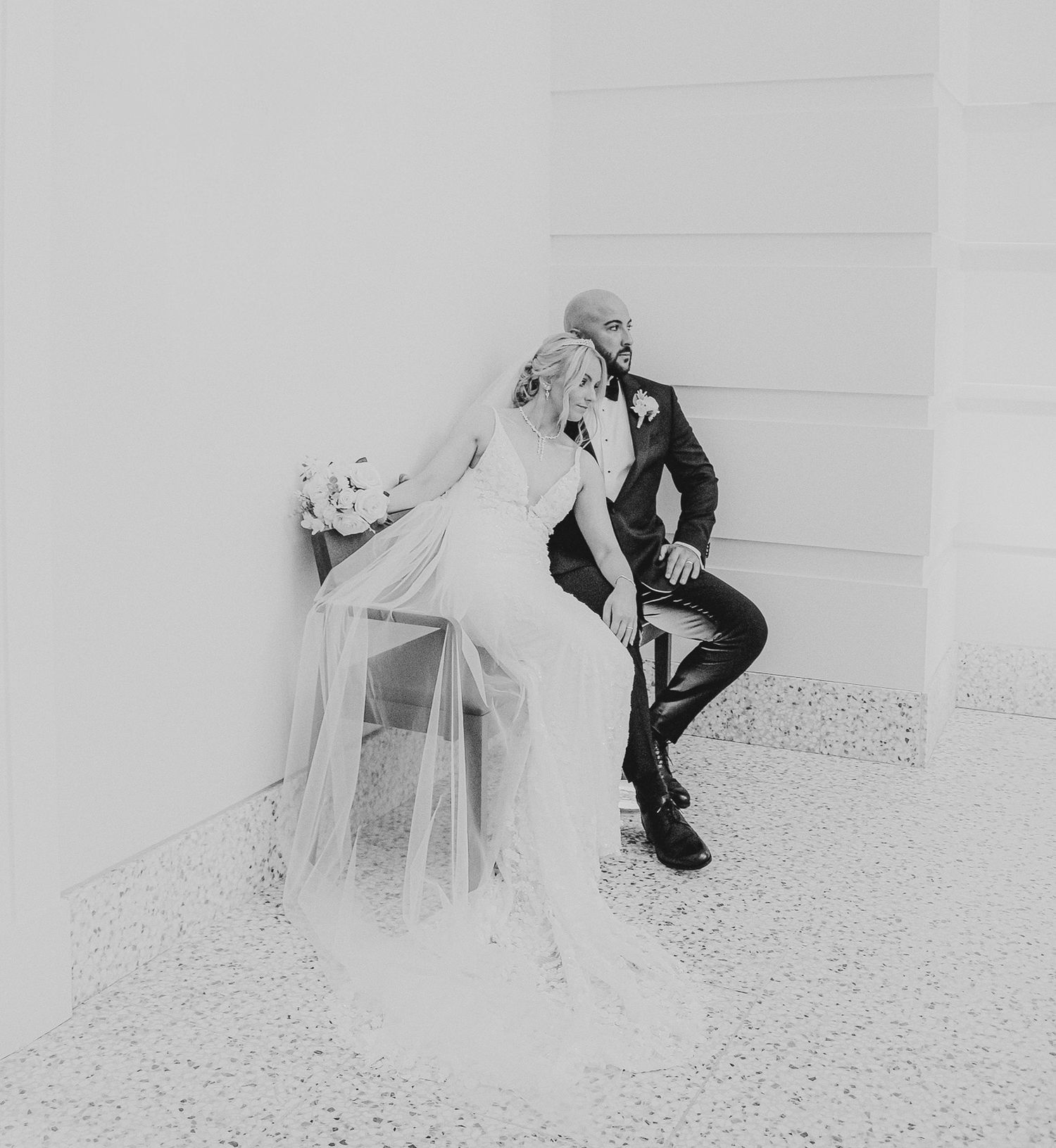 Black and white wedding portrait series showing couple in romantic poses with flowing veil against white backdrop.