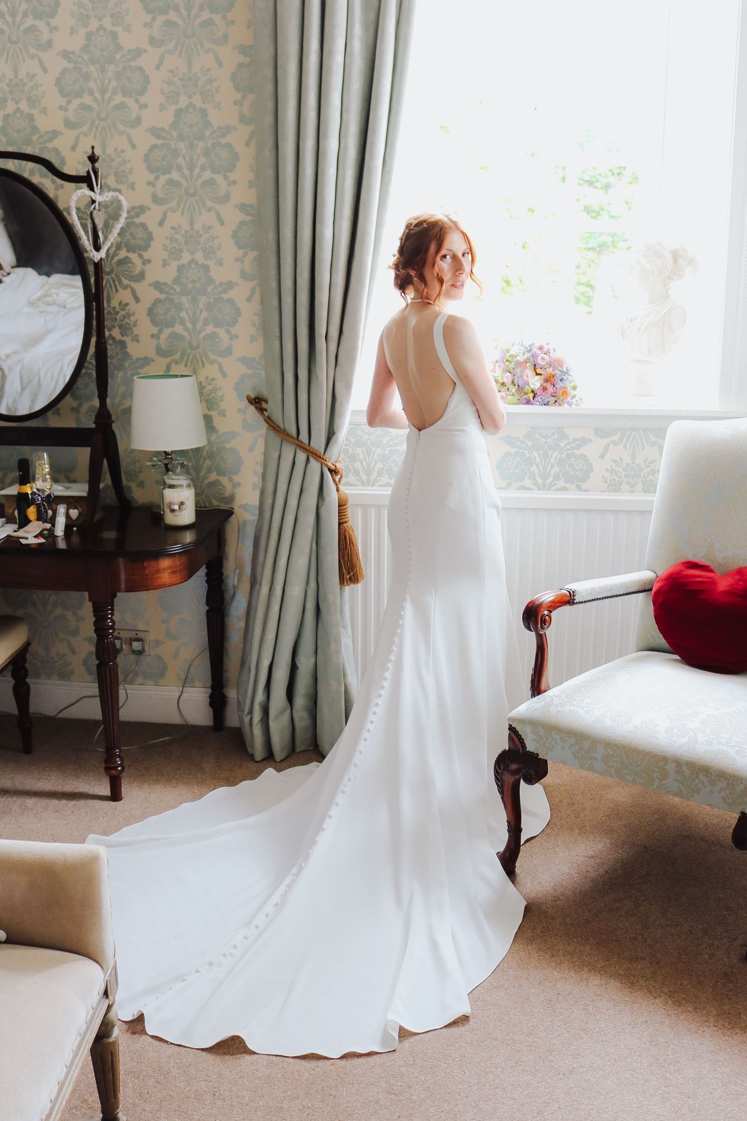 Elegant white wedding dress with flowing train shown from multiple angles in a room with damask wallpaper and natural light.