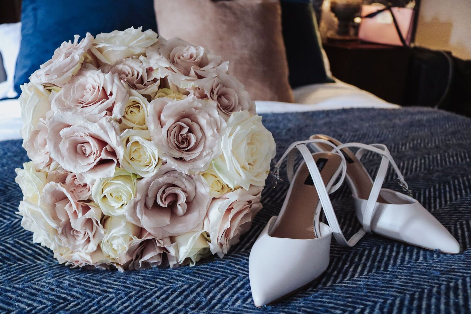 A collection of bridal details including pink and white roses, elegant white heels, and textured gray fabric.