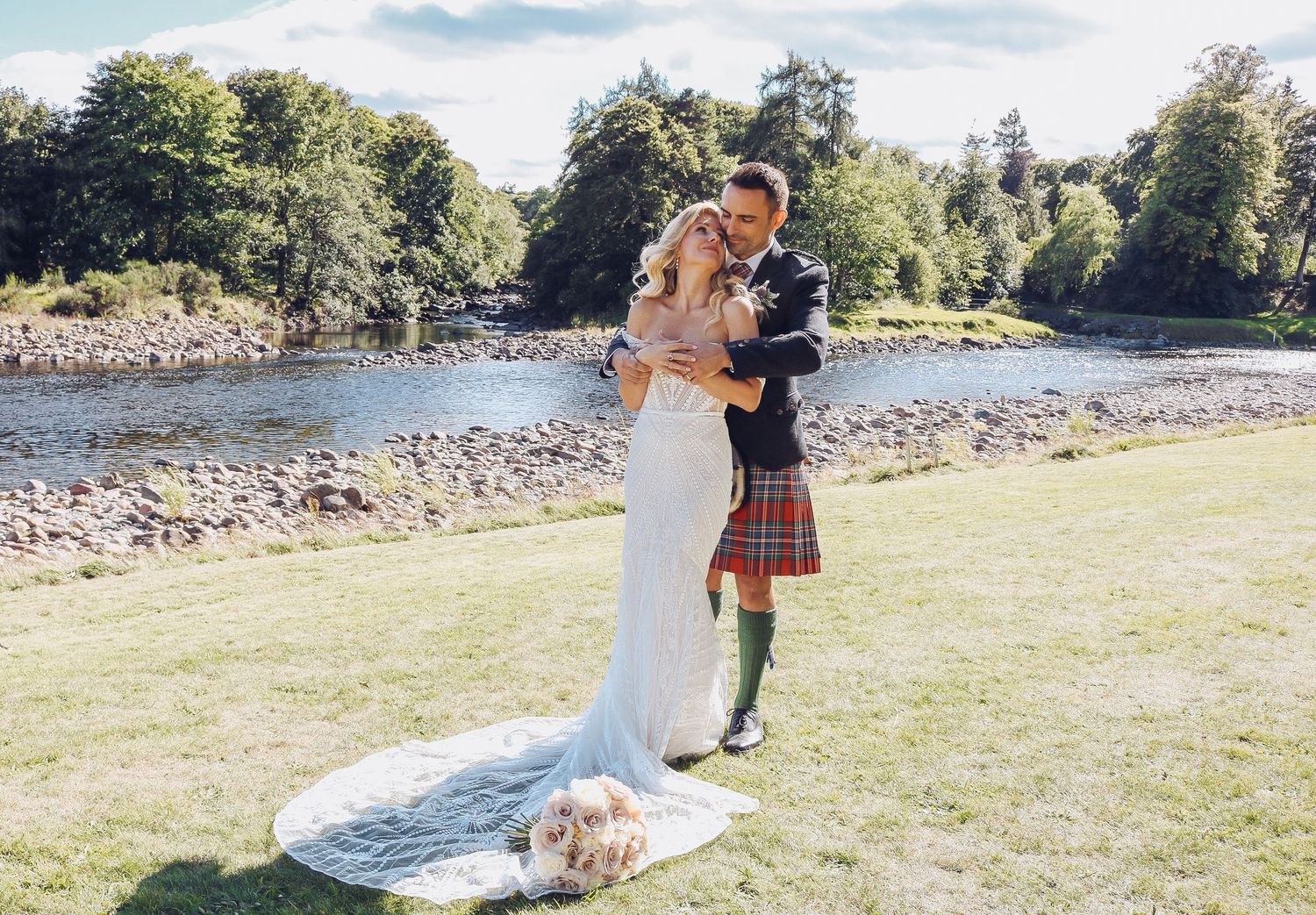 A couple in wedding attire shares a romantic moment by a scenic river on their special day.