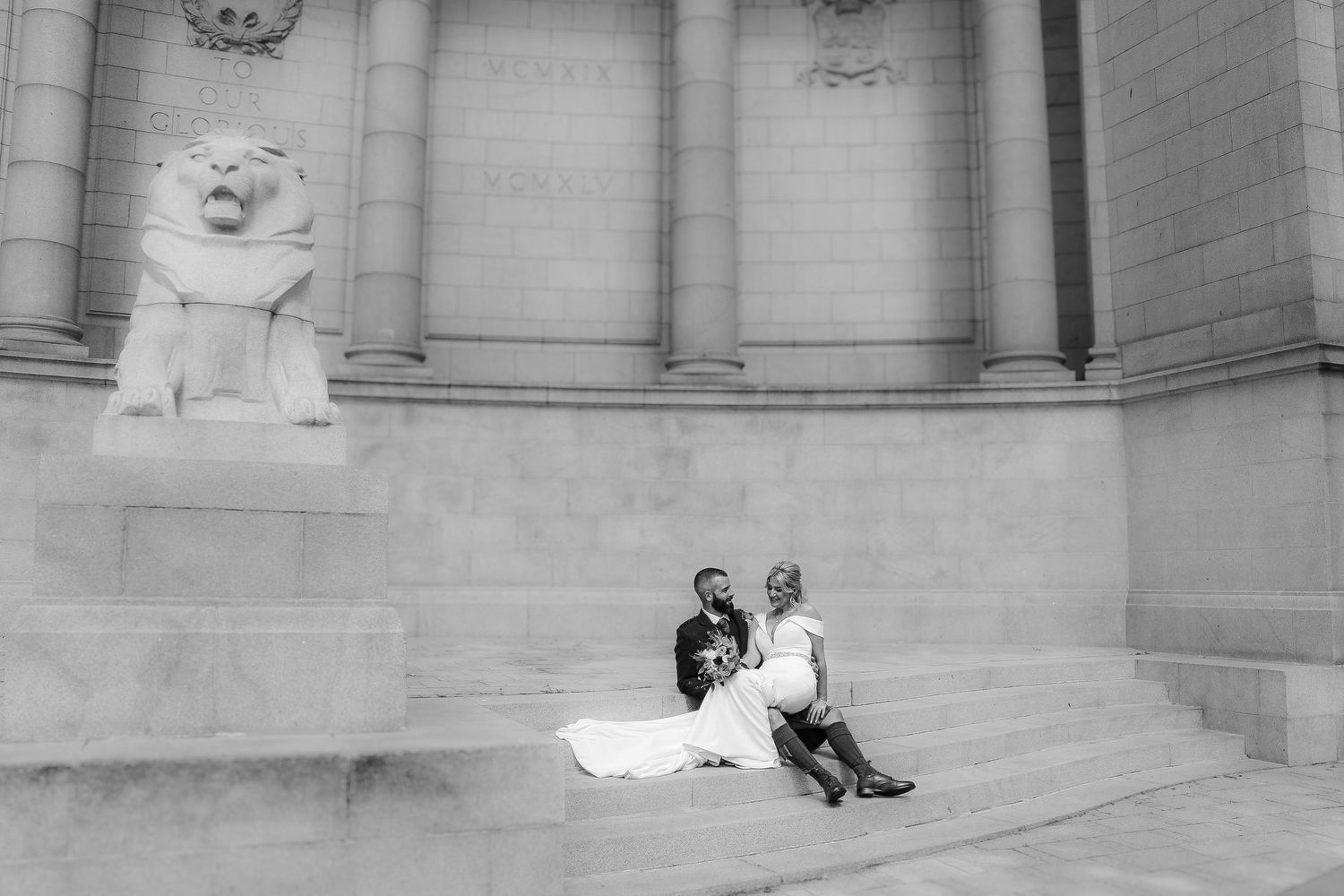 Black and white panoramic photograph showing a group of people sitting on steps of a grand stone building. Wedding-Photographer-Aberdeen-