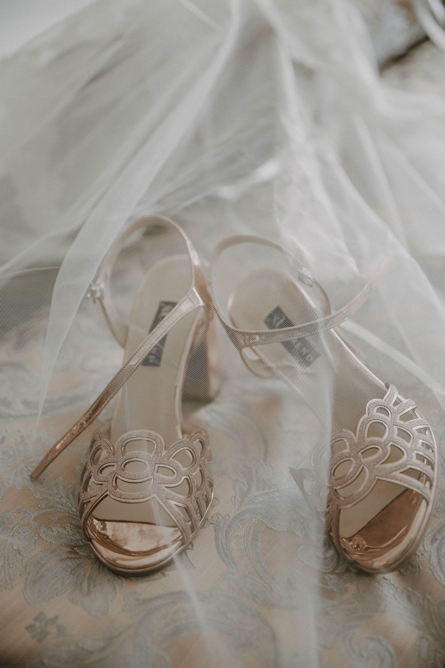 Elegant white wedding shoes with delicate floral details arranged in a row on soft tulle fabric.