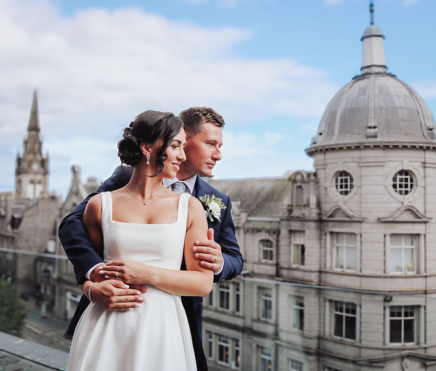 Romantic couple embraces while standing in front of historic stone buildings with ornate architecture in Aberdeen, Scotland.