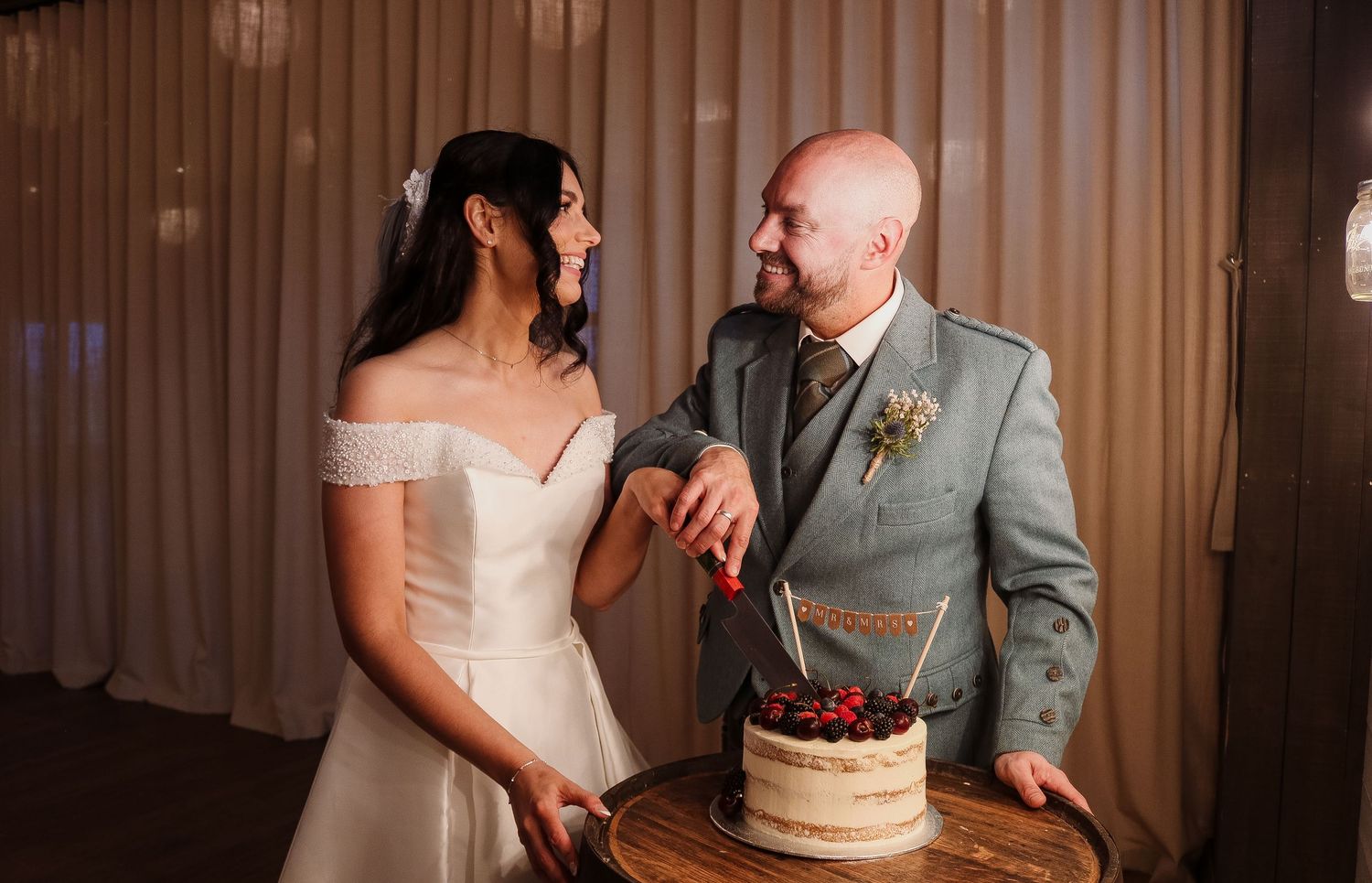A wedding couple shares an intimate moment while cutting their elegant white wedding cake at the reception.