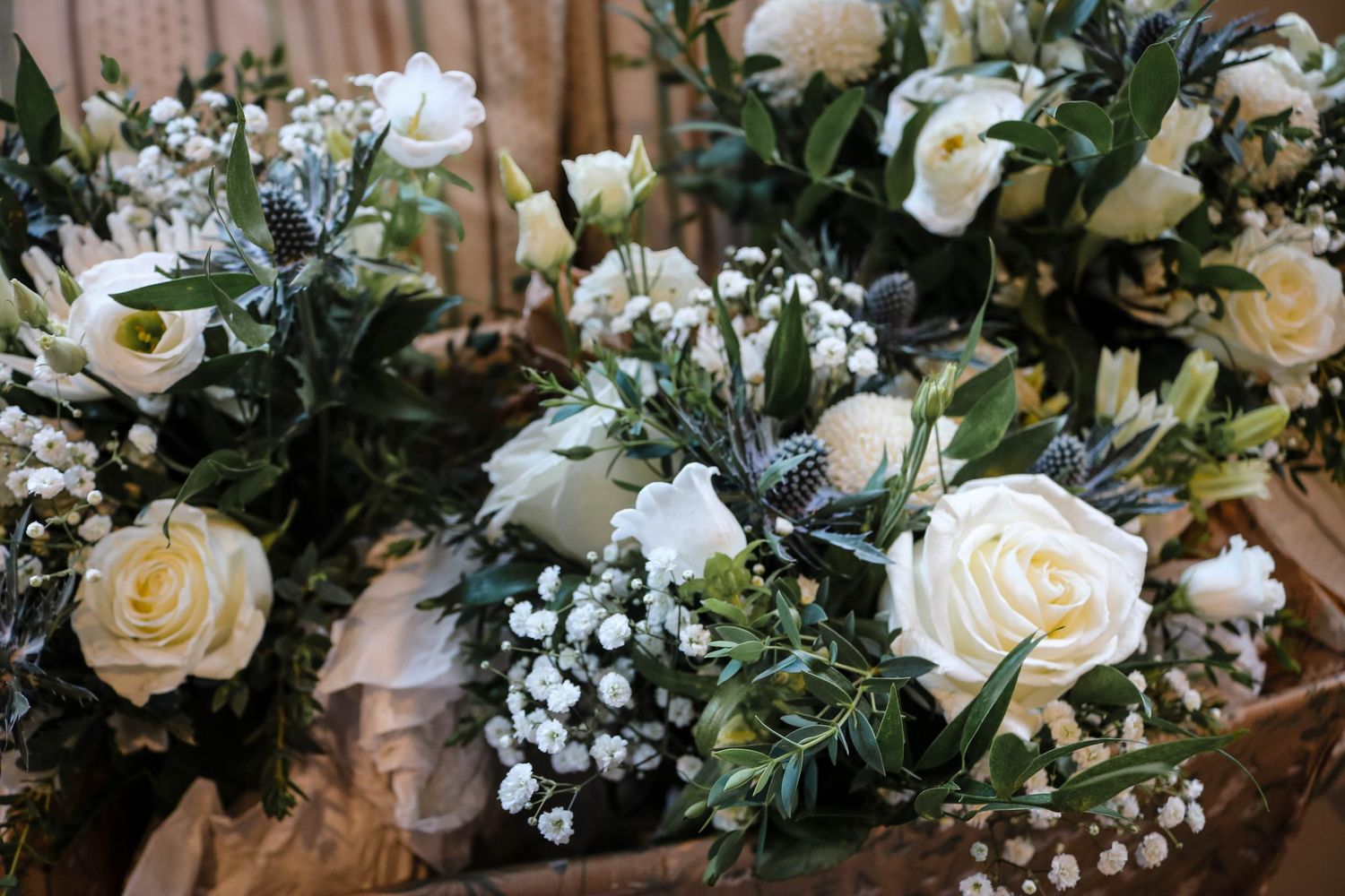 Wedding bouquet arrangements featuring cream roses, baby's breath, and green foliage on wooden surface.