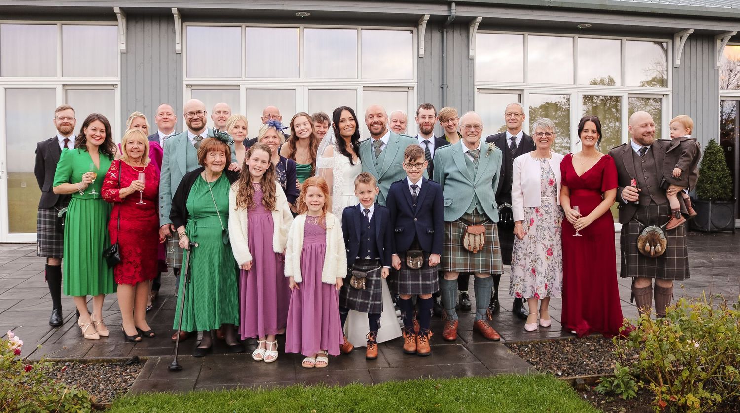 A panoramic collage of wedding party members in formal attire standing outside a building in various group arrangements.