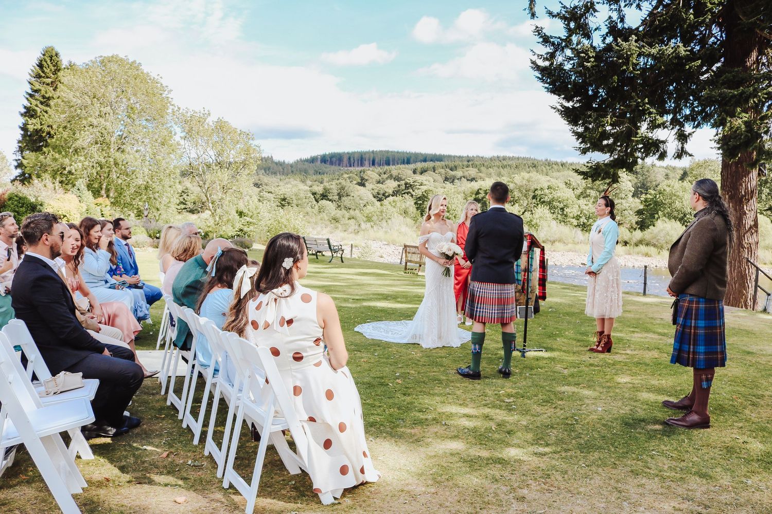 Outdoor wedding ceremony setup on a grassy hillside with white chairs and scenic mountain views in the background.