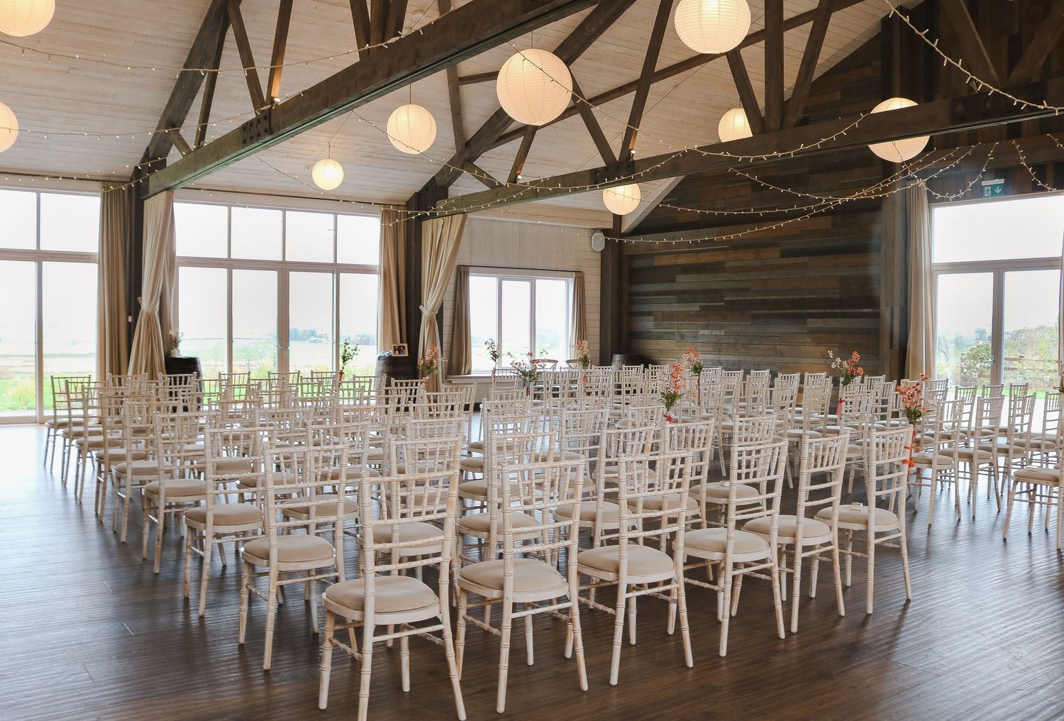 Panoramic view of an empty event venue with white chairs arranged in rows and illuminated by hanging globe lights.