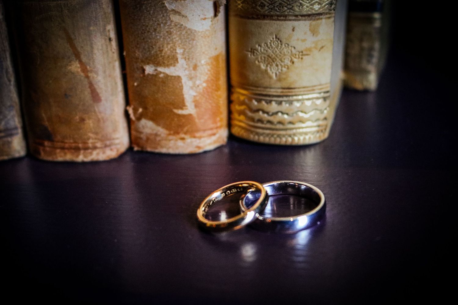 Two wedding rings on a dark surface with vintage wine bottles in the background, creating a romantic ambiance.