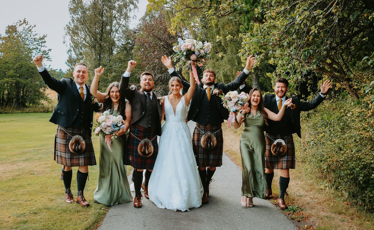 Wedding party walks along a garden path during an outdoor autumn celebration with Scottish kilts and formal attire.