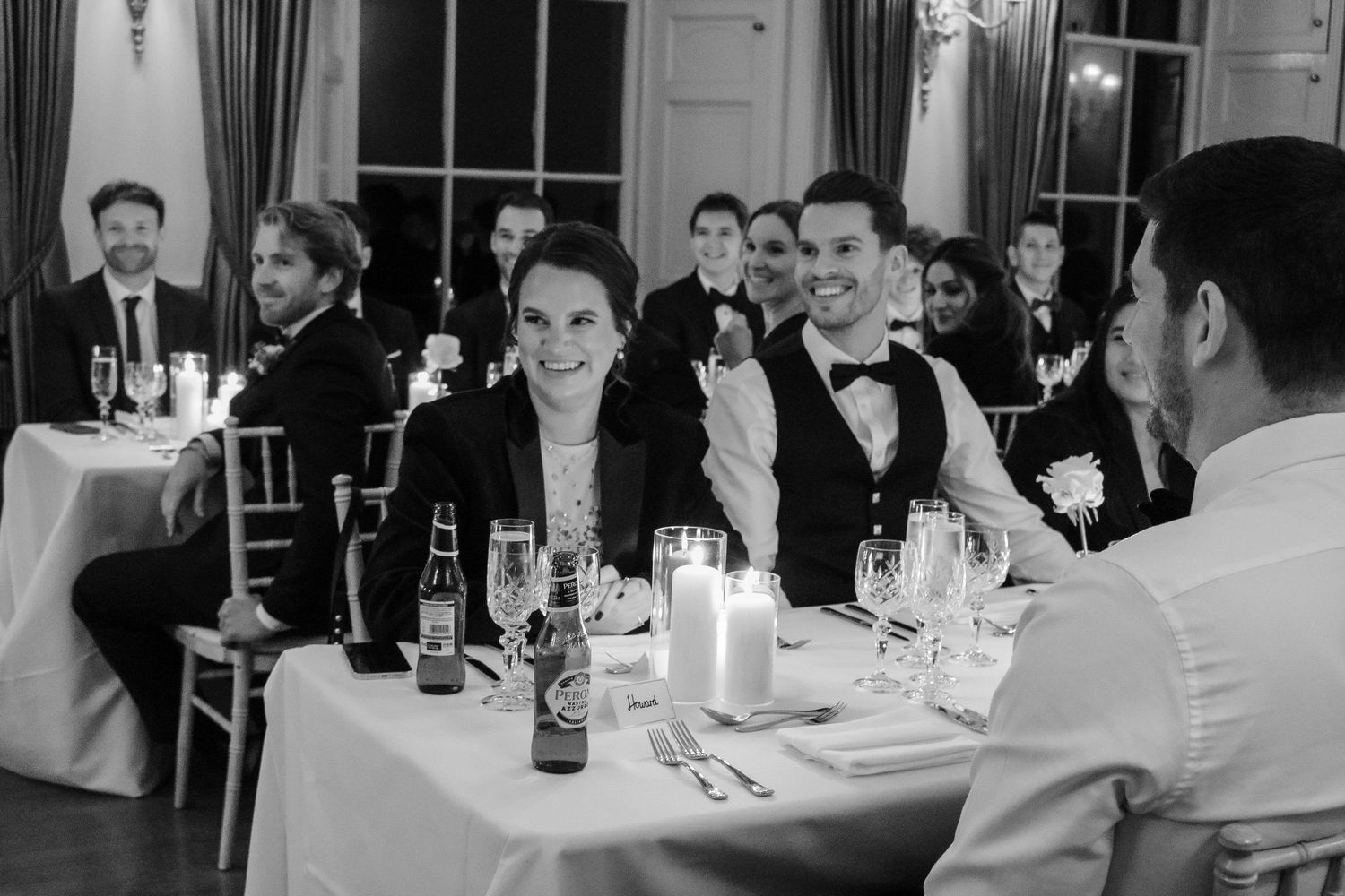 Wedding guests in formal attire enjoying lively conversation at round reception tables.