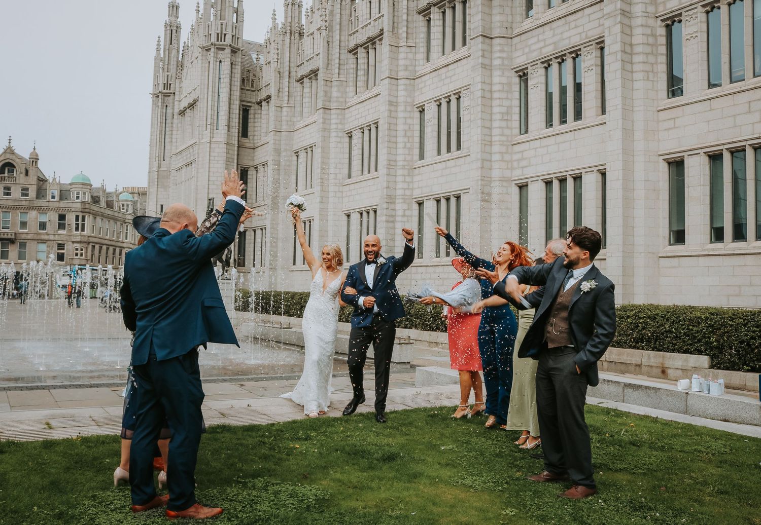 Wedding party enjoying celebratory moment outside gothic architecture building on overcast day.