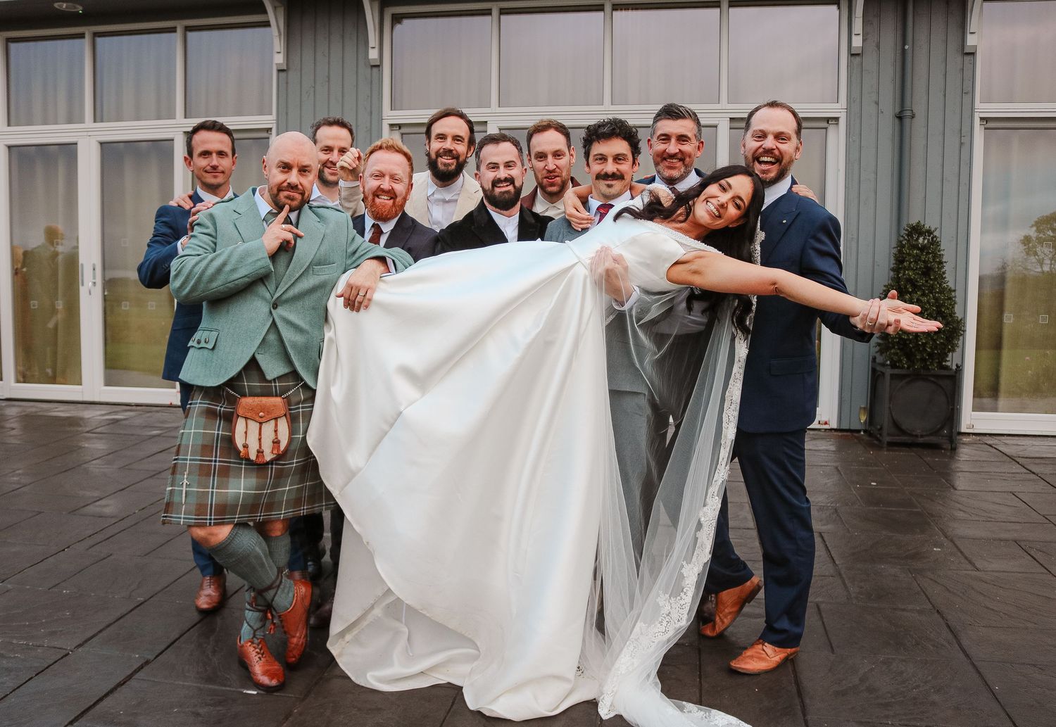A fun wedding party photo sequence showing groomsmen lifting up a white dress in playful poses on a terrace.