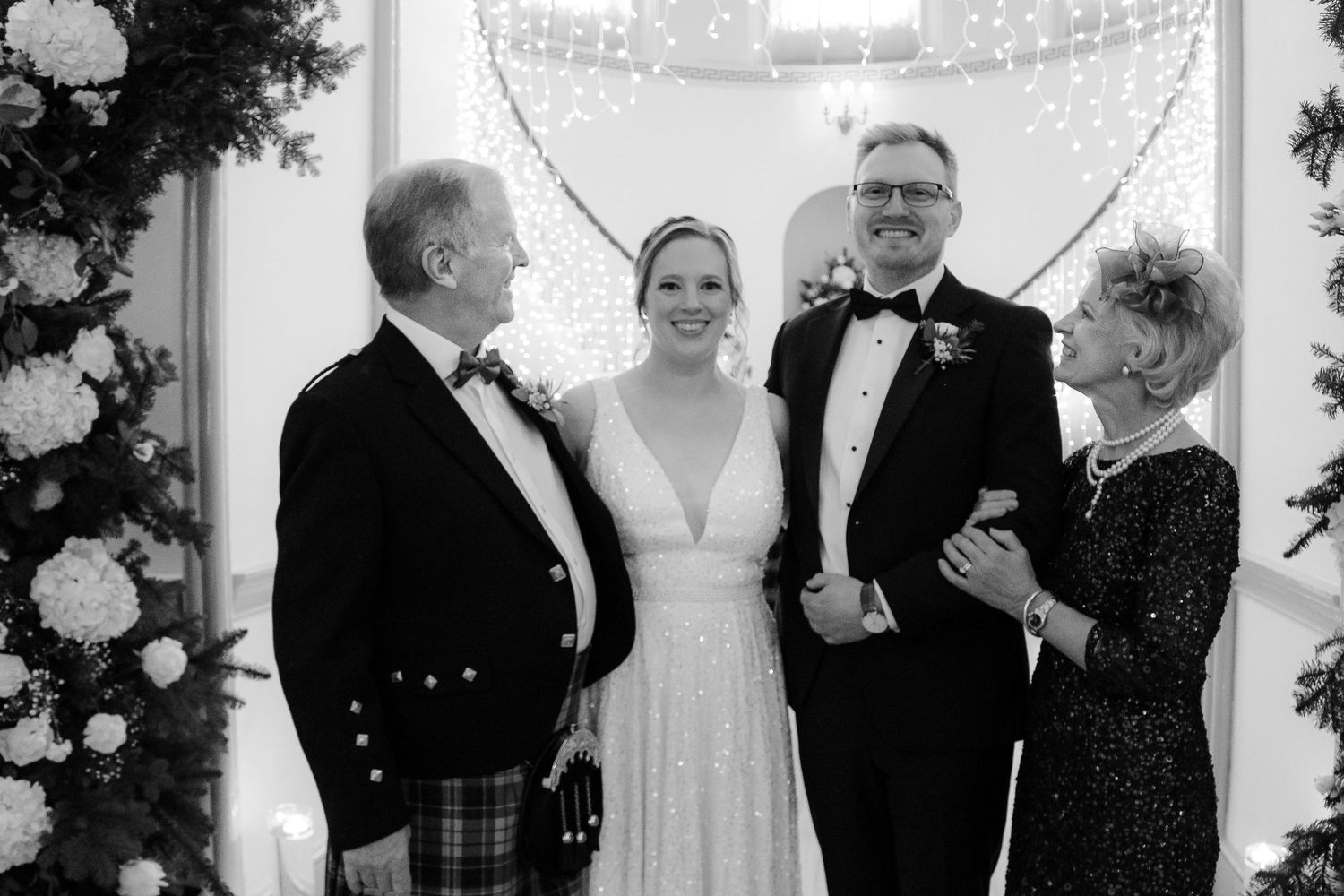 A black and white wedding photograph showing a small group in formal attire including a kilt and evening gowns.