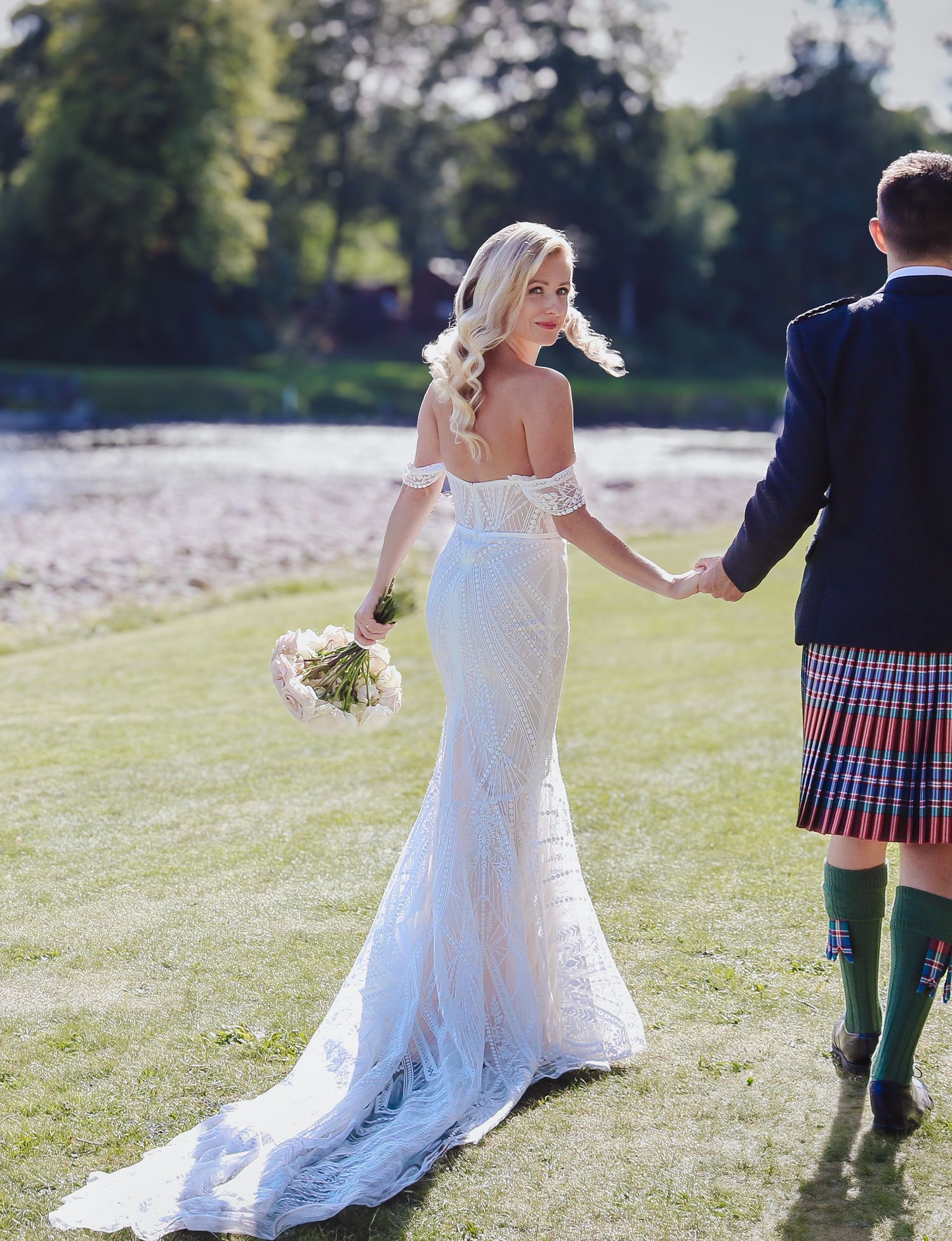 A couple in wedding attire dances and twirls on a grassy lawn during a sunny outdoor celebration.