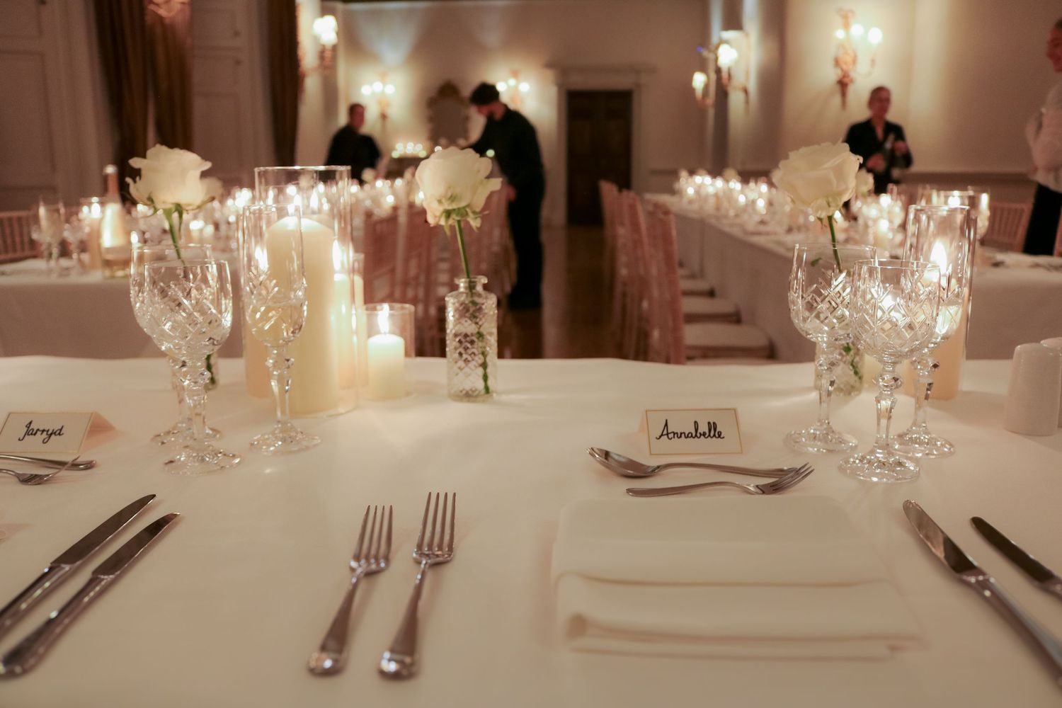 Elegant table setting at formal dinner event with crystal glasses, white linens and soft candlelight in dimly lit room.
