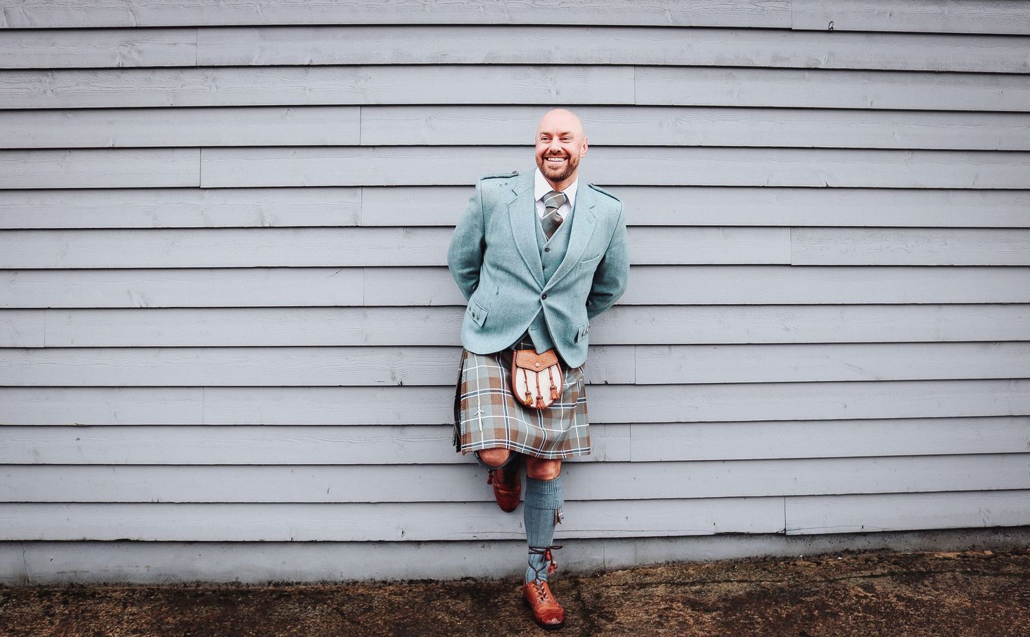 A series of six candid poses against a gray siding wall shows someone in a mint green suit and red shoes.