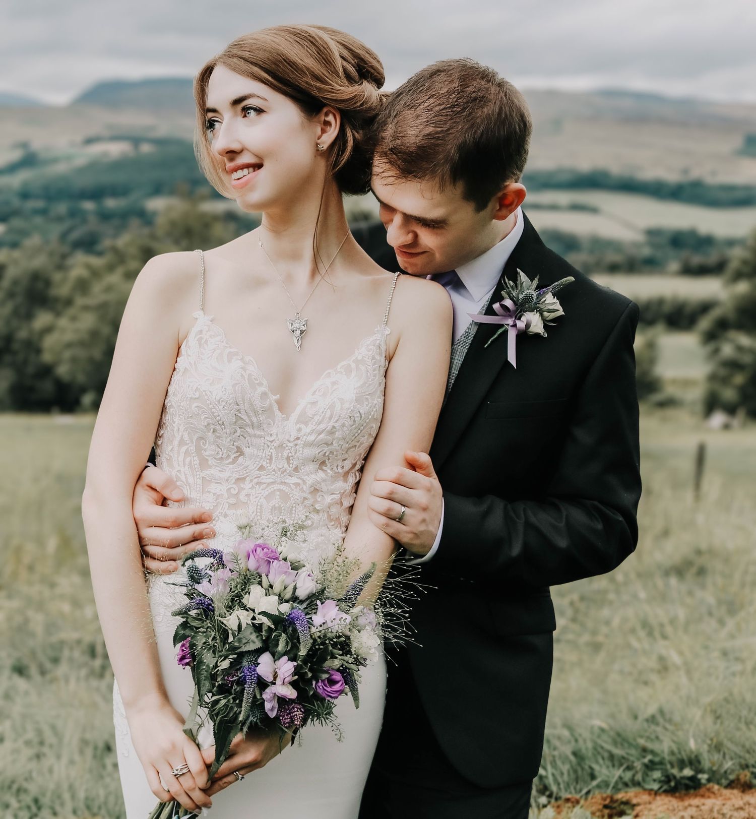 A couple shares an intimate moment in a mountain field with purple wildflowers.