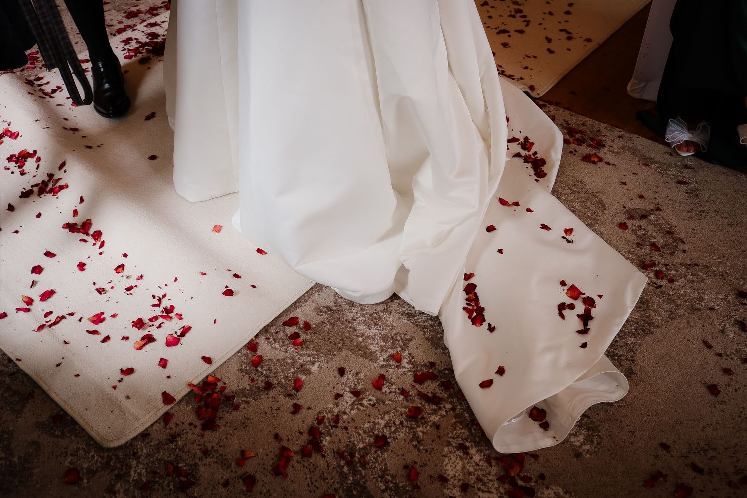 White wedding dress train spread on floor adorned with scattered red rose petals at a romantic wedding ceremony.