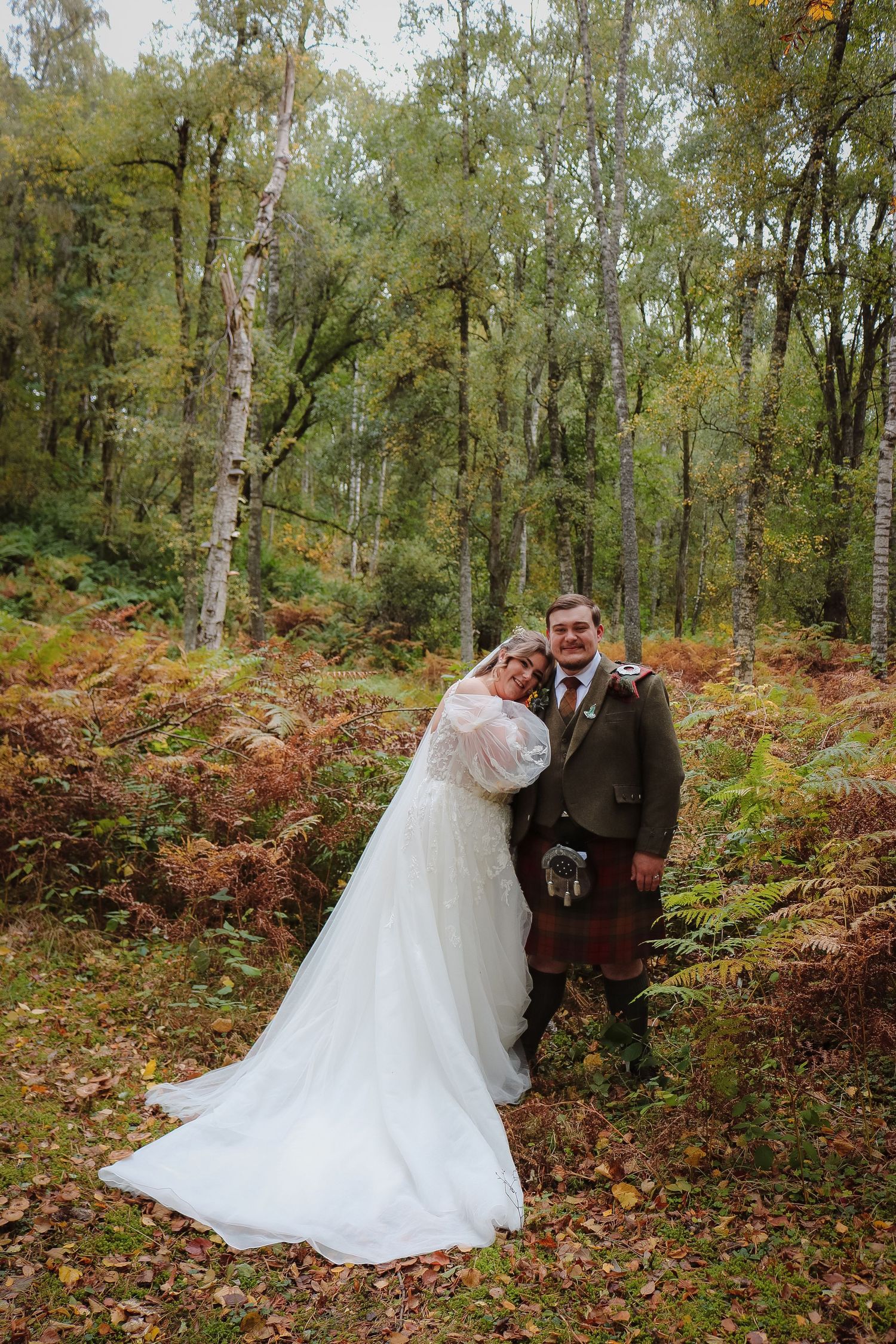 Romantic autumn woodland wedding scene at Ballogie Aberdeenshire with white gown and traditional Scottish kilt among colorful fall foliage.