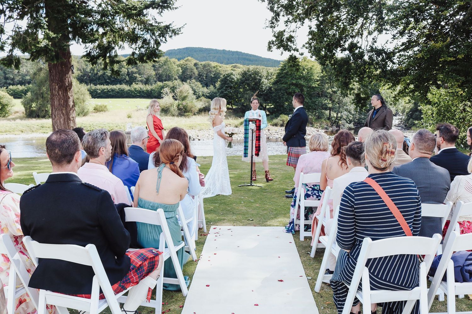 Guests seated in white chairs at an outdoor wedding ceremony with a scenic mountain view in the background.
